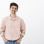 Pleasant friendly boyfriend meeting with parent. Portrait of good-looking confident man with moustache, holding hands in pockets and smiling broadly while talking with friends casually in bar.